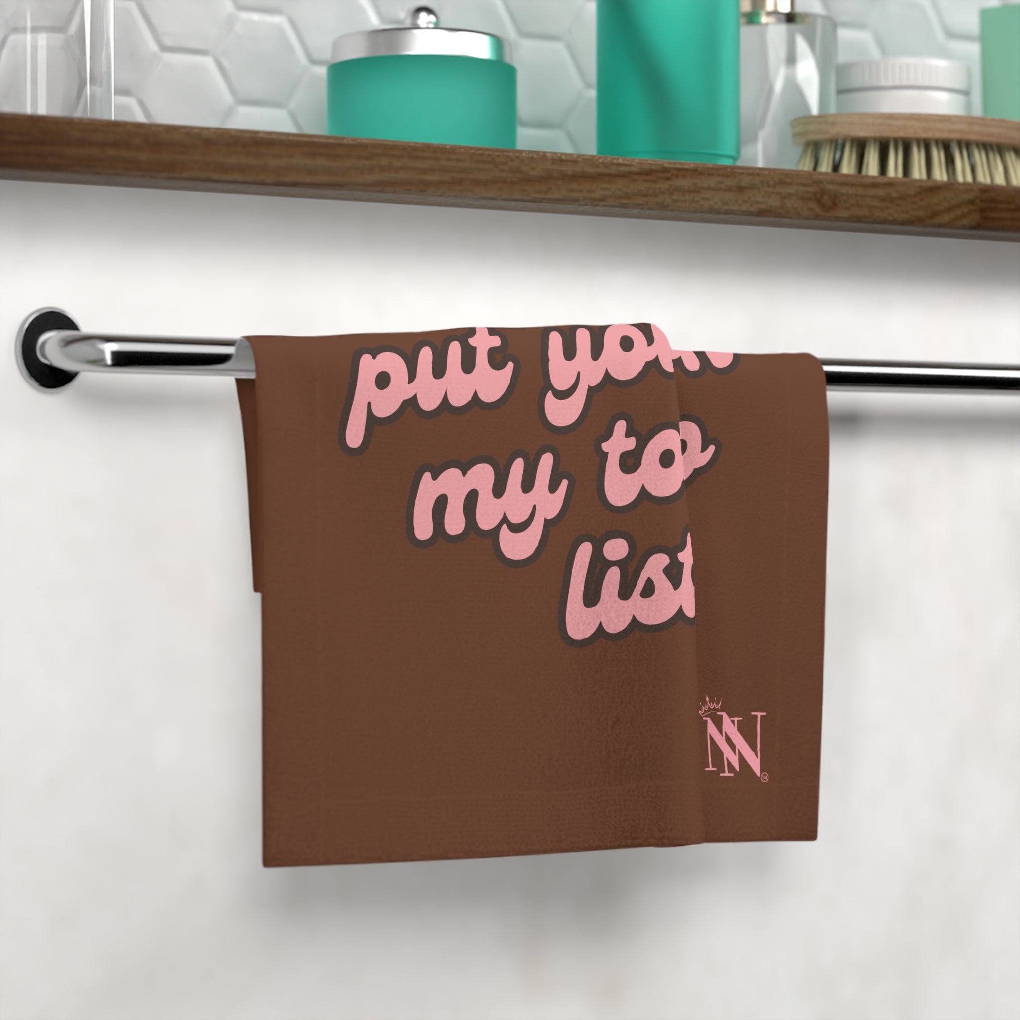 Brown hand towel with pink text 'Put You on My to Do List!' hanging on a bathroom towel rack, showcasing its playful design and practicality.